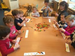 Dzieci siedzą przy stoliku bawiąc się kolorowym makaronem
