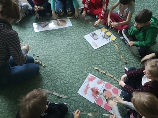Dzieci siedzą w kole układając zadania na dywanie