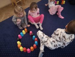 Dzieci układają kolorowe kubeczki dywanie w kształcie koła