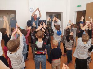 grupa dzieci tańczy podnosząc ręce do góry na przeciwko dwóch muzyków