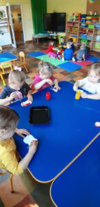 Przy stoliku siedzi czworo dzieci, które malują farbą kształt jabłka.