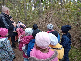 Dzieci stoją w grupce w lesie i obserwują ptasie gniazdo na krzaku