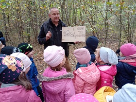 Dzieci stoją w lesie i obserwują pana, który pokazuje im dwie drewniane tabliczki