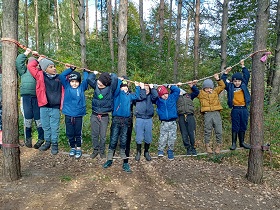 Chłopcy stoją na linie zaczepionej do drzewa i trzymają się linki, również umocowanej do drzewa