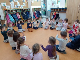 Dzieci klęczą na podłodze w kółku i poruszają rękami.