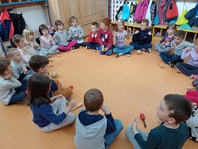 Dzieci siedzą na podłodze w kółku. Trzymają w rękach instrumenty - grzechotki i marakasy