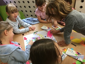 Dzieci pracują wspólnie przy stole i ozdabiają kartkę A3 pastelami