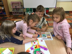 Dzieci pracują wspólnie przy stole i ozdabiają kartkę A3 pastelami