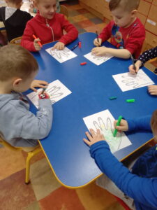 Dzieci siedzą przy stole, na obrysie dłoni rysują flamastrami zarazki.