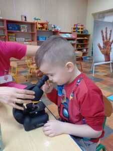 Przy stole siedzi chłopiec który patrzy przez mikroskop.