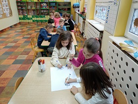 Dzieci pracują w grupach przy stołach. Każda grupa ma białą kartkę A3 i flamastry. 