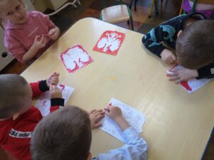 dzieci siedzą przy stole i kolorują godło Polski