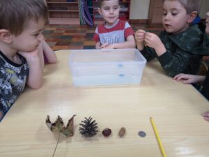 dzieci przy stoliku sprawdzają jaki przedmiot tonie, kasztan, szyszka, ołówek