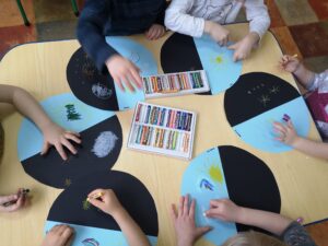 grupa dzieci siedzi przy stole i koloruje okrągłe karty pracy dzień i noc