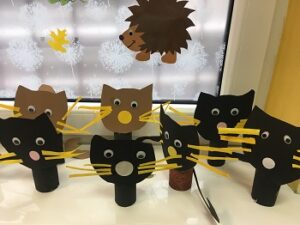 Na parapecie stoją kotki wykonane z rolek od papieru, z papierowymi brązowymi i czarnymi głowami, żółtymi wąsami, białymi nosami oraz oczami. 