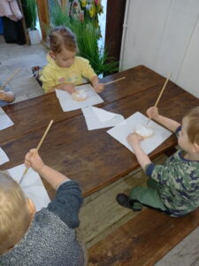 troje dzieci siedzi przy stole i maluje ozdoby choinkowe