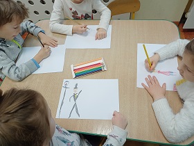 Czwórka dzieci siedzi przy stole i rysuje kredkami na białych kartkach papieru.