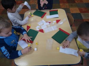 dzieci siedzą przy stole i wykonują kartki świąteczne