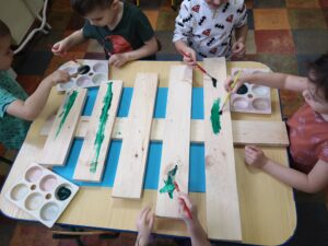 dzieci przy stole malują drewnianą choinkę