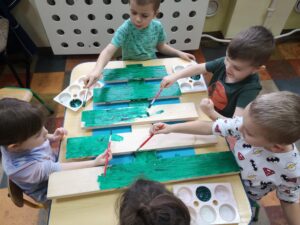dzieci przy stole malują drewnianą choinkę