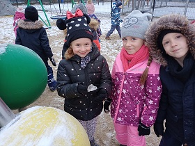 Trójka dzieci stoi na placu zabaw. Jedna dziewczynka trzyma w ręku lód.