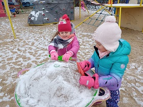 Dwie dziewczynki czyszczą łopatkami zabawkę ze śniegu.