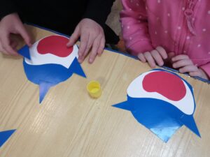 dziewczynki układają sylwetę rekina z papieru