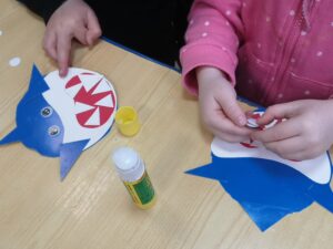 dziewczynki układają sylwetę rekina z papieru