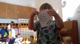 Chłopiec trzyma w ręku kartkę z narysowanym słoneczkiem i z napisem: Jesteś super.