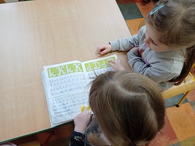 Dwie dziewczynki oglądają książkę o kaligrafii. Na stronie są napisane literki K i D.