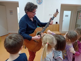 Dzieci podchodzą do pana z gitarą i dotykają jej strun.