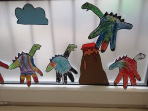 na oknie naklejone papierowe dinozaury