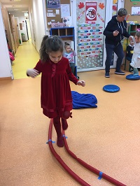 Dziewczynka podąża po torze przeszkód. Ma na sobie czerwoną sukienkę.