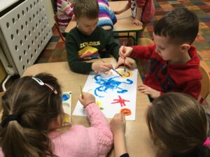 czworo dzieci maluje wspólnie farbami na jednym kartonie