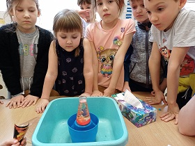Dzieci obserwują co się dzieje w naczyniu stojącym przed nimi na misce.