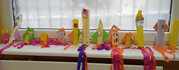 Na parapecie znajdują się rakiety dzieci, wykonane z papieru kolorowego z wiszącymi kawałkami bibuły i ze świecącymi elementami.