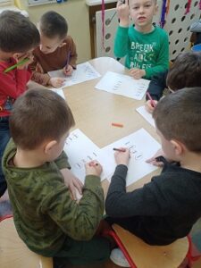 Dzieci siedzą przy stoliku i zaznaczają flamastrami napisy na kartkach.