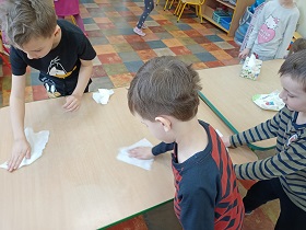 Chłopcy sprzątają stoły, wycierając je białymi chusteczkami. 