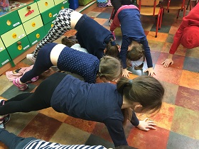 Dzieci wykonują kocie grzbiety na podłodze w sali.