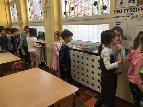Dzieci przyglądają się rzeczom ułożonym na parapetach pod oknami.