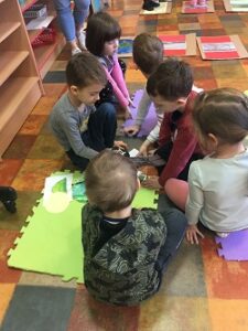 Dzieci siedzą w małych grupkach i układają elementy na kolorowych planszach.