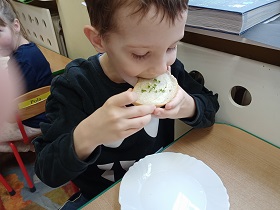 Chłopiec je chleb z kiełkami. Na stole leży biały talerz.