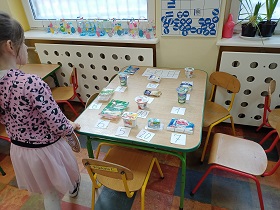 Dziewczynka stoi przed stołem, na którym umieszczone są różne opakowania z cenami.