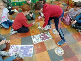 Dzieci układają duże monety na podłodze. Na podłodze znajdują się również duże banknoty o nominale 10 i 20 złotych.