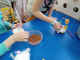 Ręce dzieci sypią nasiona do koszyczków, w których jest włożona wata.