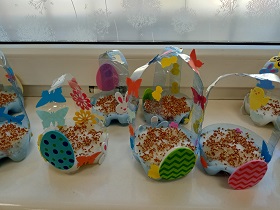 Wielkanocne koszyczki stoją na parapecie. Są ozdobione naklejkami pisanek, motylków i króliczków. W środku koszyczków wyłożona jest wata z nasionami.