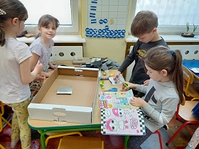 Trzy dziewczynki i chłopiec pracują przy stoliku i wycinają elementy z kolorowych gazet.