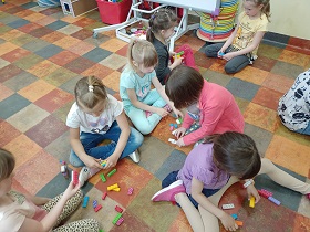 Dzieci siedzą na podłodze w parach. Przed sobą mają klocki, które układają.