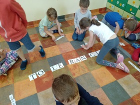 Dzieci są na podłodze i układają napis z liter. Napis: tolerancja.