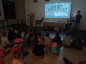 Dzieci siedzą na podłodze i oglądają film o świecie zwierząt na tablicy.